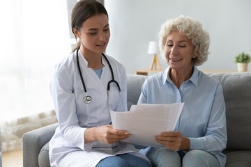 Smiling older woman patient and young doctor reading insurance contract