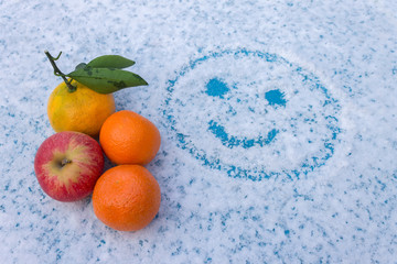 A set of fruits lies on a snowy table with a painted, smiling face © Николай Чекалин