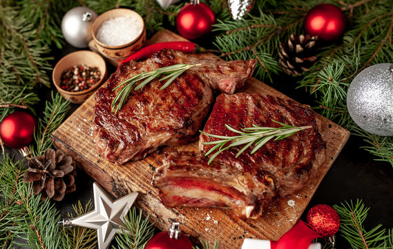 Christmas dinner for two, grilled beef steak ribeye, herbs and spices on a stone table with a Christmas tree and New Year's toys