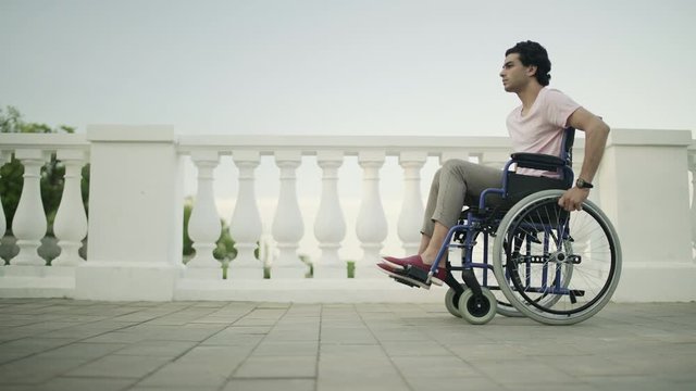 Young man in a wheelchair rides along a path in a public garden.