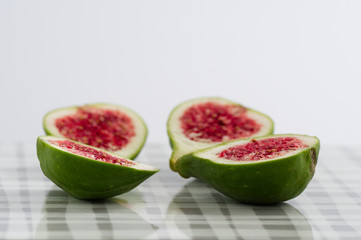 vier halbe feigen aufgeschnitten mit rotem fruchtmark und grüner schale liegen auf einem brettchen vor weißem Hintergrund