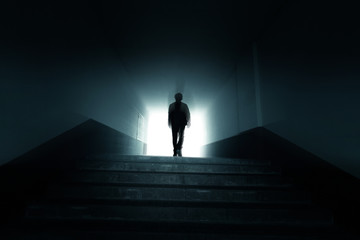 Man walking to the light in the dark tunnel. - obrazy, fototapety, plakaty