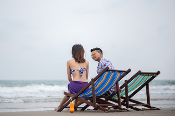 Couple Sitting On Chair At Beach Against Sky