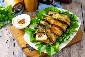 Tasty fish baked with vegetables in eggplant, served with paprika yogurt sauce on a wooden table. Copy space.