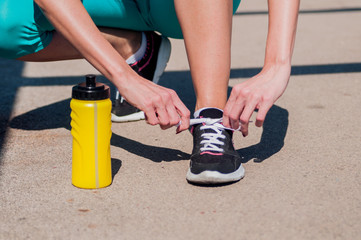 Fit woman tying her laces before a run. Female runner tying her shoelaces while training outdoor on a road. Unrecognizable young runner tying her shoelaces