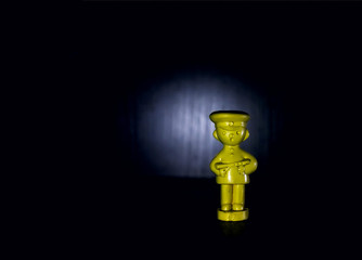 Yellow, plastic soldier of the USSR on a black background, illuminated by a car "headlight".