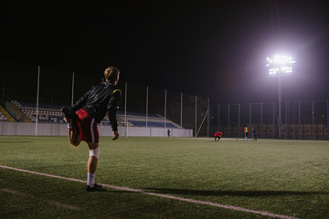 football player doing warm up exercises on the field before the match at night