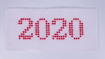 on a white canvas from a fabric in a hole, numbers two thousand twenty are embroidered with red...