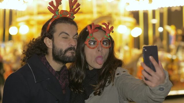 Happy funny young lovers taking funny selfie at Christmas- outdoor