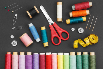 Colored thread coils, scissors, buttons, needles, pin and a tailor meter on a black background. The...