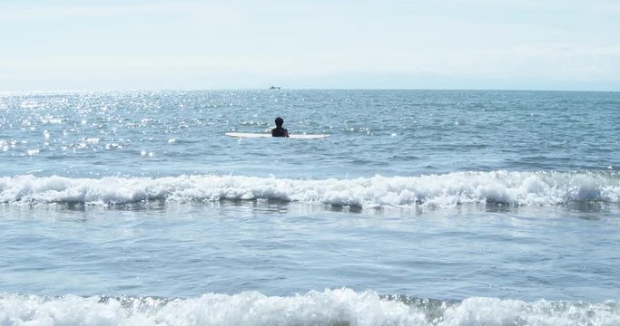 A young male surfer with his surboard in the sea waiting for the waves. Enoshima, Japan.