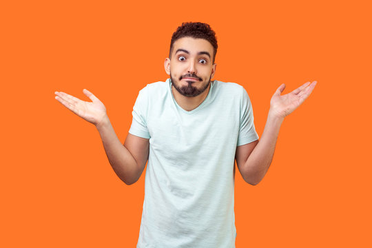 I don't know, who cares. Portrait of confused clueless brunette man with beard in white t-shirt shrugging shoulders, making no idea gesture, whatever. indoor studio shot isolated on orange background