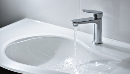 Chrome tap with open water that flows into a white modern sink - obrazy, fototapety, plakaty