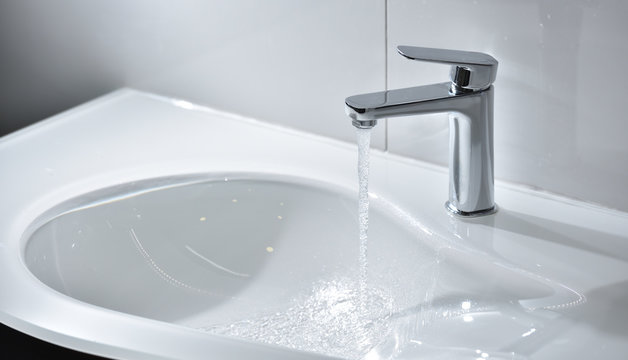 Chrome tap with open water that flows into a white modern sink