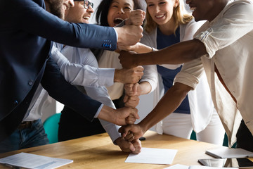 Overjoyed younger older mixed race teammates making pyramid of fists.