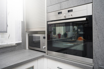 Metallic microwave and oven in gray kitchen interior