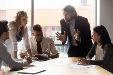 Serious young businessman leaning over table, explaining ideas to teammates.
