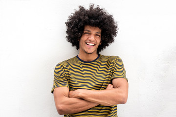Cool young man with afro hair smiling with arms crossed by white background