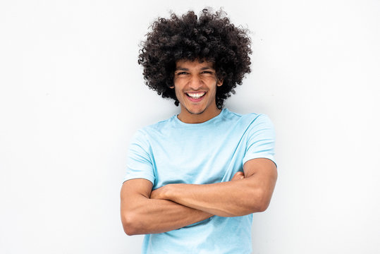 handsome young man with afro hair and arms crossed smiling by white background