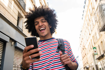Close up happy young arab guy with afro hair looking at cellphone in city and laughing