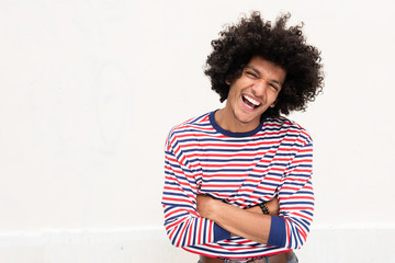 cool young happy North African man with afro hair laughing with arms crossed against white...