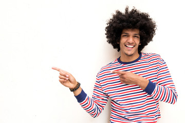 cool young arab guy with afro hair and pointing fingers to copy space on white background