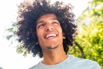 Close up handsome young North African man with afro hair smiling outside
