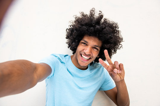 happy young North African man taking selfie against white background with peace hand sign