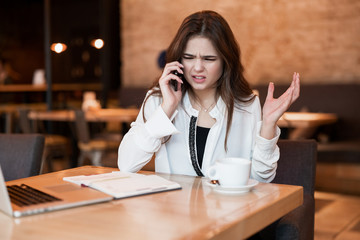 young woman having unpleasant phone conversation working outside office in her laptop during lunch break drinking hot coffee in cafe looking irritated modern businesswoman