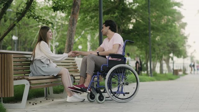 Happy disabled man in a wheelchair and his girlfriend meets in the park