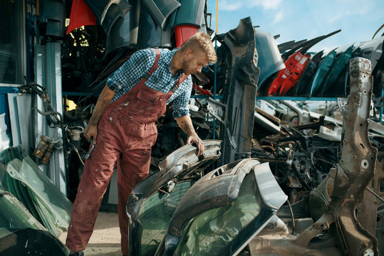 Male repairman choosing spare parts on car junkyard