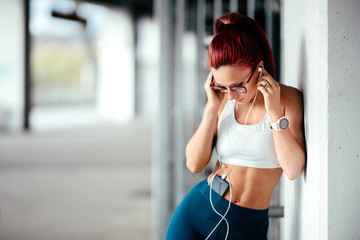 Portrait of athletic girl working out, resting and stretching while listening to music