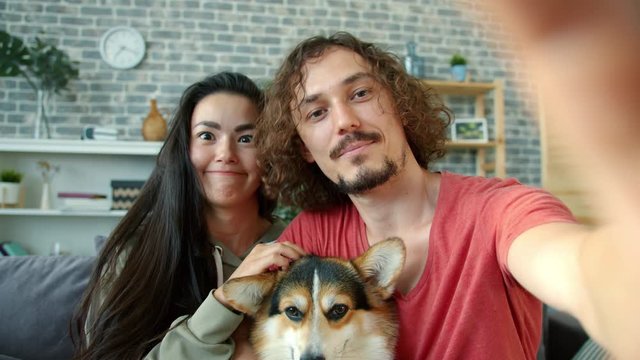 POV of happy family Asian girl and Caucasian guy taking selfie with corgi dog posing smiling having fun at home together. Technology and happiness concept.