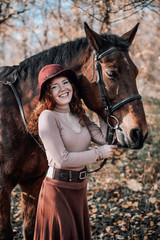 Portrait of beautiful red haired woman with horse outdoors.