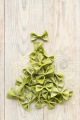 pasta with spinach in the form of bows on wooden table in the shape of Christmas tree