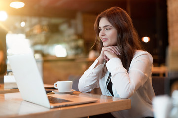 young beautiful woman in white stylish jacket working in her laptop outside office during coffee...