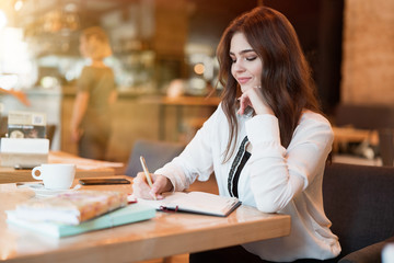young beautiful woman in white stylish jacket working on project outside office writing in planner during coffee break in cafe modern businesswoman multitasking