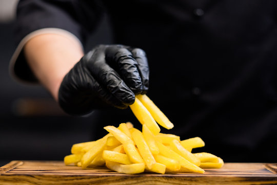 Traditional American fast food restaurant snacks. Cropped shot of chef in cooking gloves serving french fries on wooden board.