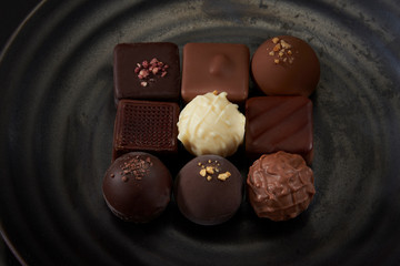 A pile of exquisitely beautiful chocolate cubes placed on a dark grey ceramic plate with a water ripple.