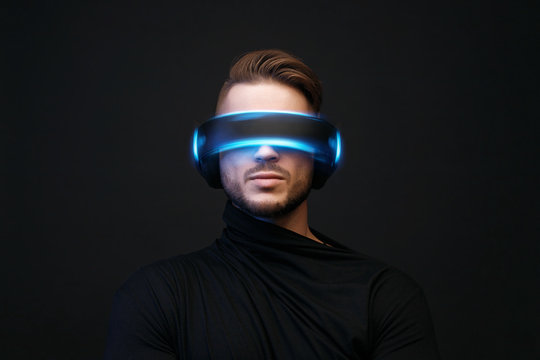 Model young man with beard in glasses of virtual reality on dark background. Augmented reality, future technology concept. VR. Blue neon light.