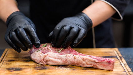 Steakhouse kitchen. Cropped shot of chef cooking Cowboy steak, seasoning raw beef bone in meat on wooden board.