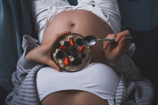 cropped image of pregnant woman in bed with oatmeal with berries, healthy Breakfast in bed, healthy pregnancy