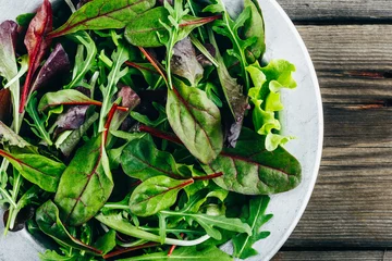 Fototapeten Mix of fresh green salad leaves with arugula, lettuce, spinach and beets on wooden rustic background. © nblxer
