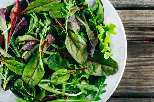 Mix of fresh green salad leaves with arugula, lettuce, spinach and beets on wooden rustic background.