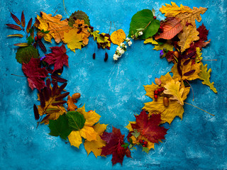 Autumn composition. Heart-shaped frame of fallen green, yellow, orange and red leaves on a turquoise background. Autumn, leaf fall. Flat position, top view, copy space