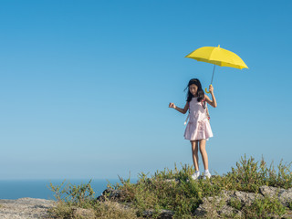 Girl with backpack holding yellow umbrella climbing on the top of city view, lifestyle concept.