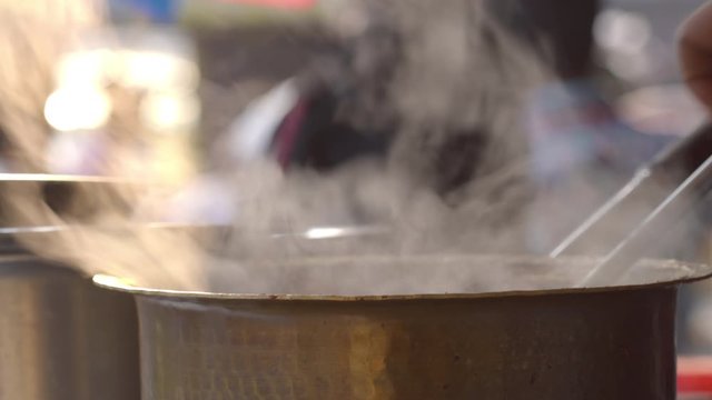 Tea or Chai being prepared and mixed / stirred in a vessel / utensil at a chai stall in the evening