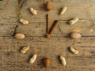 Clock made of different nuts and cinnamon on wooden background. The clock strikes one. Hours of proper nutrition