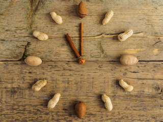 Clock made of different nuts and cinnamon on wooden background. The clock strikes eleven o'clock. Hours of proper nutrition