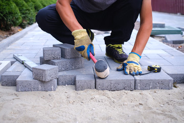 The master in yellow gloves lays paving stones in layers. Garden brick pathway paving by...